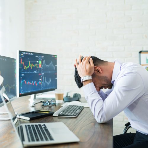 Side view of stressed young broker sitting with head in hands at desk while working from home